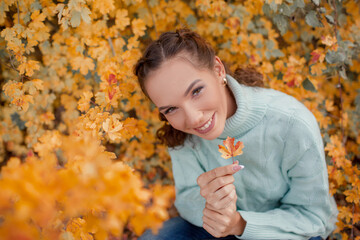 Portrait of a beautiful woman  hold the fall leaves and resting in the park. The happy girl wearing...