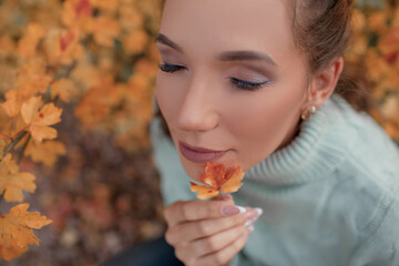 Portrait of a beautiful woman  hold the fall leaves and resting in the park. The happy girl wearing...