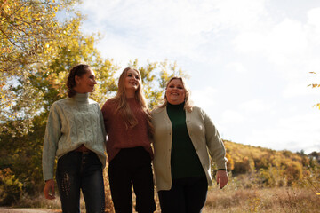 Multiracial female people  with different bodies and hairs walking in the fall parks together.  Friends wearing warm fashion clothes, knitted sweaters.