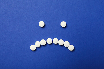 Sad emoji from pills on dark blue background, top view