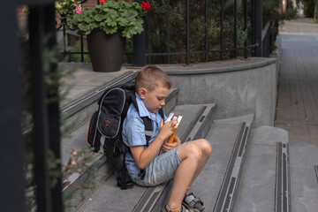 Obraz premium a school boy with school books in his hands sits on the steps of the school