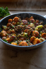 Rustic meal with pan fried potatoes, carrots, onions, chives and minced pork in a hot and steaming frying pan