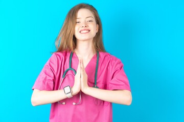 Young caucasian doctor woman wearing medical uniform praying with hands together asking for forgiveness smiling confident.