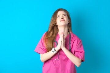 Young caucasian doctor woman wearing medical uniform begging and praying with hands together with...