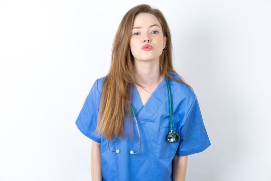 Shot of pleasant looking Young caucasian doctor woman wearing medical uniform , pouts lips, looks at camera, Human facial expressions