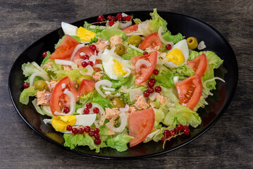 Lettuce salad with tuna, boiled eggs, vegetables on black dish