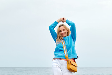 Attractive blond woman in light blue hoodie walking on winter beach. Traveling. Wellbeing and harmony concept. Unity with nature.