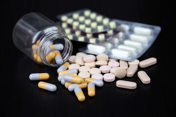 Different pills on a black wooden table, variation of medication in capsules. Background for pharmacy, antibiotics, vitamins