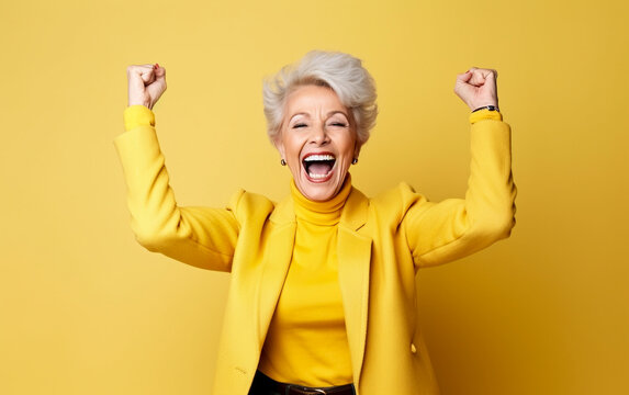 A elderly woman exultation with his fists raised and a joyful expression - isolated on yellow background