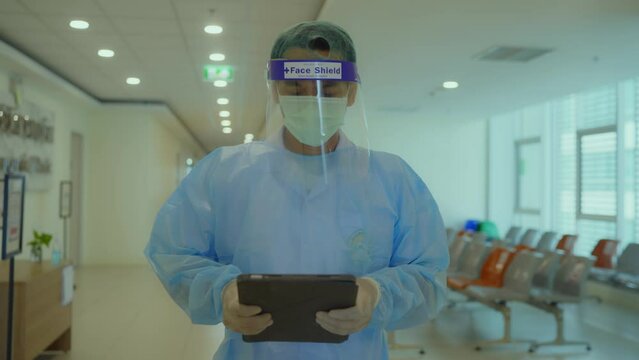 A doctor with a tablet in his hands walks along the hospital corridor. The doctor walks along the corridor of the modern clinic. A doctor in a protective suit