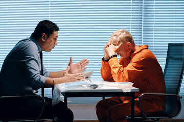 Emotional detective talking to penitent criminal in interrogation room