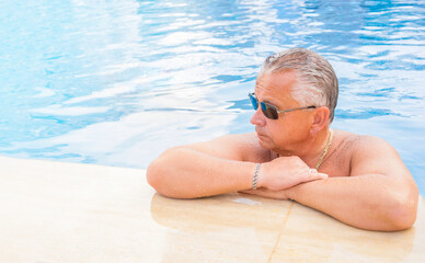 Senior man wearing sunglasses in an outdoor pool. Healthy lifestyle, active lifestyle of adults.