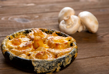 Julienne in a pot and mushrooms  on a wooden  table. Mushrooms baked with cheese crust in pan  .top view