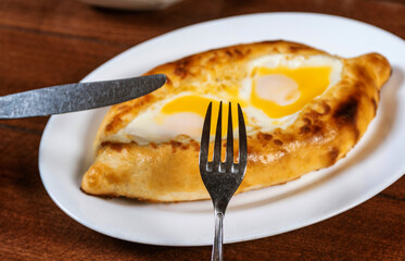 Man eating adjar Khachapuri. Georgian national pie khachapuri with egg and cheese in the white plate  on wooden background.