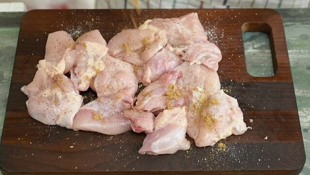 The chef sprinkles cumin on the chicken pieces.
