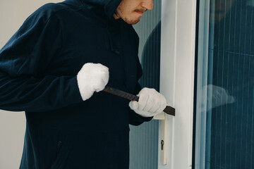 Cropped image of burglar with crowbar breaking door, he is entering house for stealing in daytime