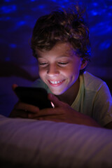 Cheerful boy sending text message on smartphone at night