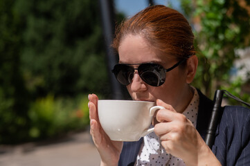 Blind woman in business suit drinking coffee in outdoor cafe. 