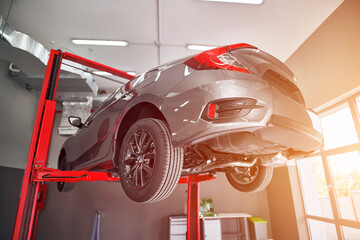 The car is being lifted up by a hydraulic machine for a technician. Close-up modern japanese car.
