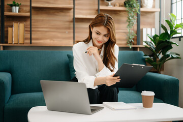 Young beautiful woman using laptop and tablet while sitting at her working place. Concentrated at work. in living room on the sofa at home office.