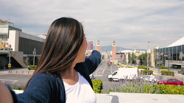 Happy handsome woman smiling relaxed and looking at camera in the street taking a selfie. Relaxed happy lady laughing and staring and holding the camera standing outdoors with a city landscape behind.