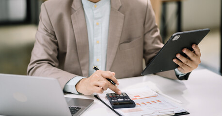 Serious young man sit at workplace desk in office use calculator calculates monthly expenses, taxes, personal budget management concept