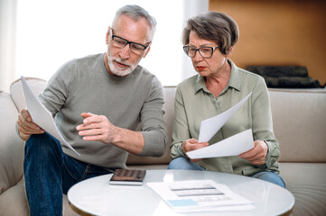 mature couple holding current expense document and fill tax form