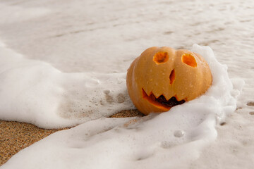 Smiling halloween pumpkin in the ocean on the beach in summertime