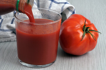 Verser du jus de tomate dans un verre avec une tomate en gros plan