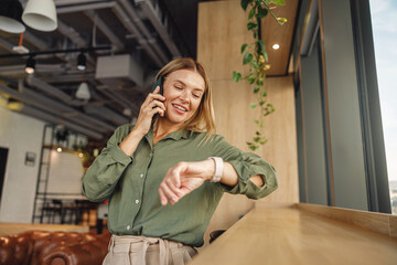 Woman manager looking on her wrist watch during phone conversation with client in coworking