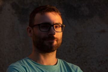 Portrait of a man looking at the camera, with beard and glasses, a bit hipster, in the shadows of the sunset