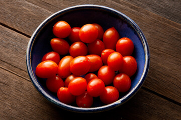 A blue cherry tomato bowl above a real wooden table in top view