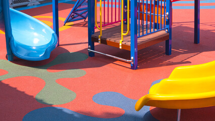 Yellow and blue slides with playground climbing equipment on colorful rubber floor in outdoors...