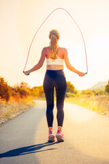 woman wearing sportswear and jumping at skipping rope on sunrise - obrazy, fototapety, plakaty