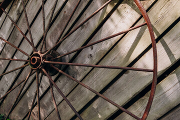 An old rusty wheel from a large cart against the background of a dilapidated unpainted fence. Abandoned place of rural type with a rusty wagon wheel close-up