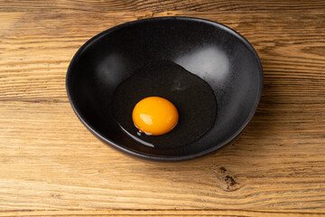 One Broken Egg in Black Bowl, Raw Yolk and White, Fresh Broken Organic Chicken Egg