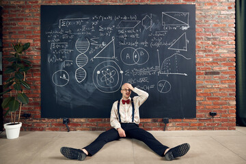 Young man, teacher, scientist sitting in despair and stress by blackboard with scientific...