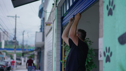 Person closing local storefront garage. Man sliding down business facade in sidewalk