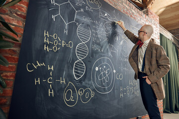 Young bald man, scientist, professor standing by blackboard with chemical formulas and...