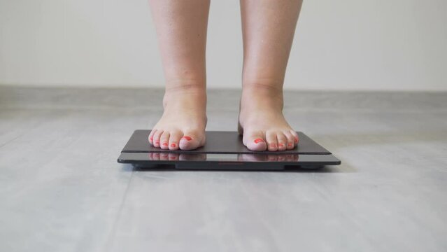 Adult well-fed woman stands on floor scales. Weighing fat woman with red manicure. Healthy lifestyle and diet. Proper nutrition and weight loss. body positive lady. Body fat control. Pound, kilogram