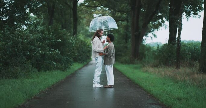 Young queer couple standing in the middle of the road under an umbrella. 