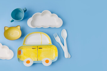 Cute children's plates and dishes shape of a car, clouds on blue background. Creative serving for baby. Concept of kids menu, nutrition and feeding.