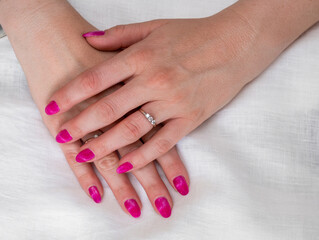 Close-up of well-groomed female pink nails. Beautiful clear fingers of a young girl with nice manicure and Glitter Nail Polish. Girl hands on a white background. Girl is wearing two diamond rings.