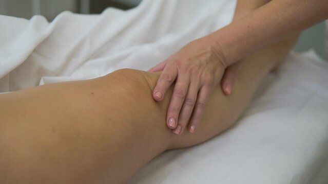 A masseuse makes a foot massage for an adult fat woman. Lymphatic drainage. Women's hands do a massage of the hips, calves, feet, knees. Massaging, stroking, pressing, kneading movements of the finger
