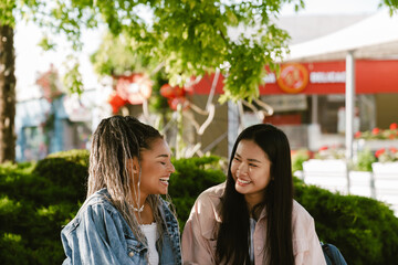 Two joyful women talking while spending time together outdoors at street