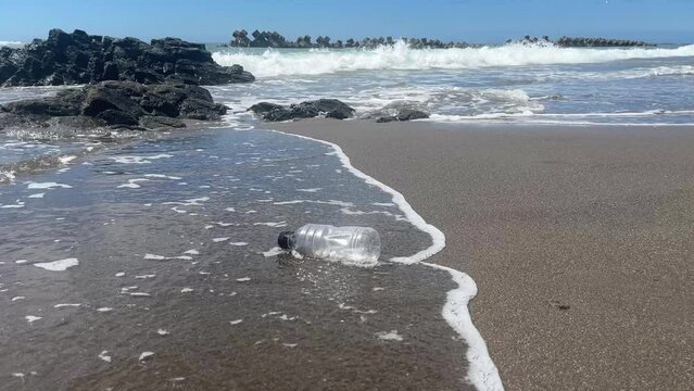 One empty plastic bottle floating off a sandy beach into the sea on a summer day