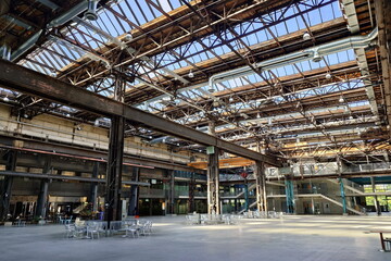 Large empty interior space of former heavy industry factory space. Large windows, beams, and rusted...