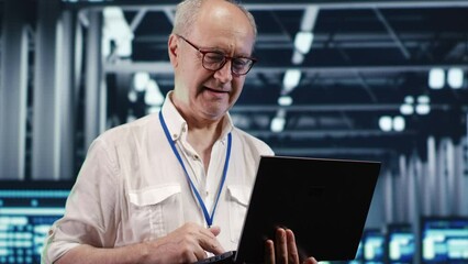 Qualified IT professional navigating network of servers in industrial location. System administrator with laptop ensuring seamless operations, doing optimizations and maintenance in data center