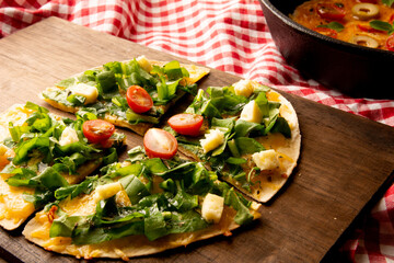 Arugula handmade pizza served in wooden cutting board above a wooden table with a red picnic cloth