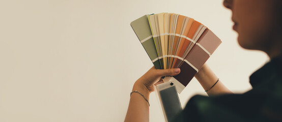 Woman choosing color using swatch catalog standing near wall.